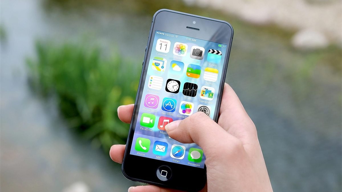 Mão segura um iPhone com a tela inicial aberta, mostrando os ícones de Calendário e Mail