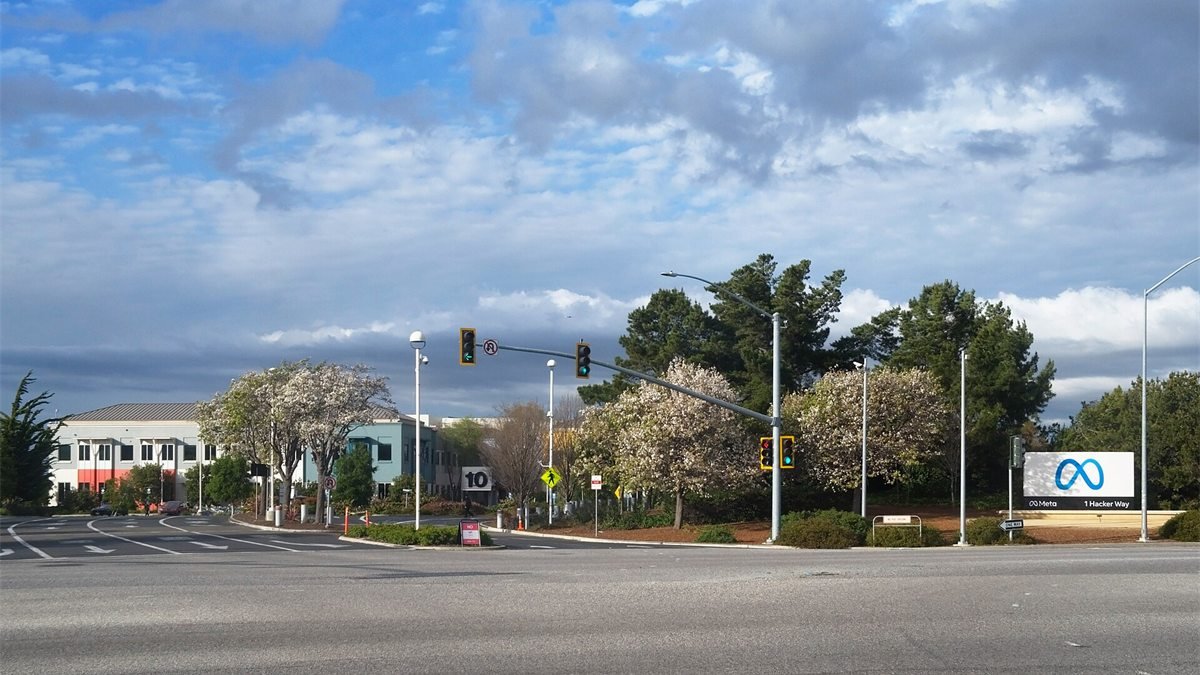 Cruzamento em frente à sede da Meta em Menlo Park, na Califórnia, com a placa da empresa e o endereço 1 Hacker Way