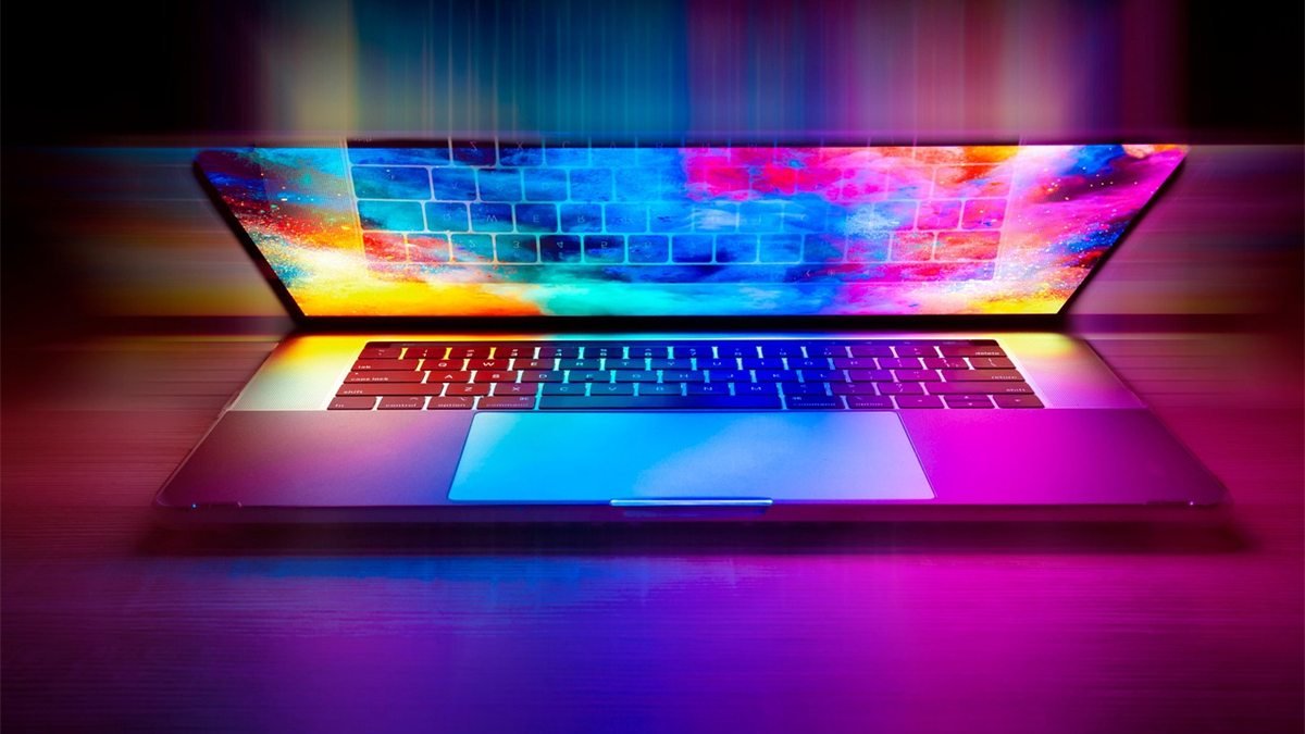 Notebook aberto sobre uma mesa, com tela e teclado iluminados por luzes coloridas