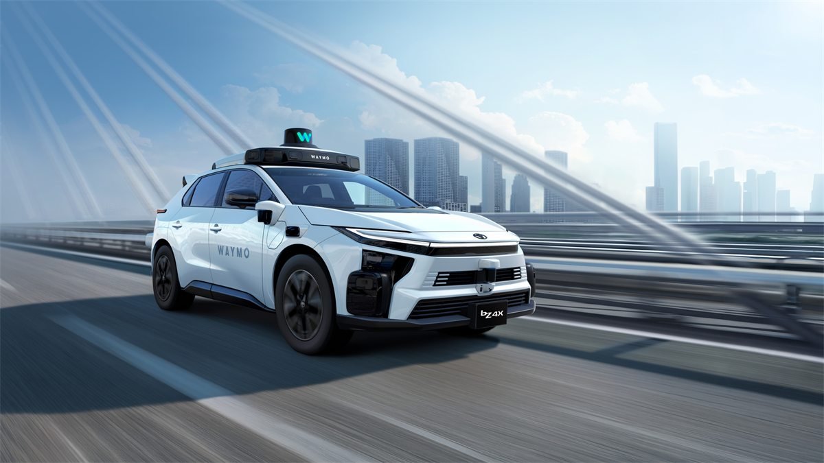 SUV elétrico Toyota bZ4X branco com a marca Waymo e sensores no teto, rodando numa ponte com prédios altos ao fundo